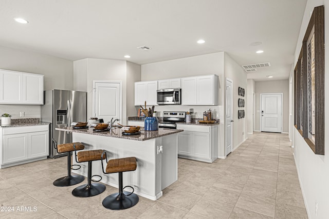 kitchen featuring appliances with stainless steel finishes, dark stone counters, a kitchen breakfast bar, white cabinetry, and a kitchen island with sink