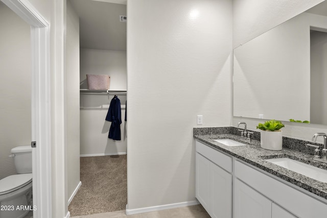 bathroom with toilet, double vanity, and baseboards