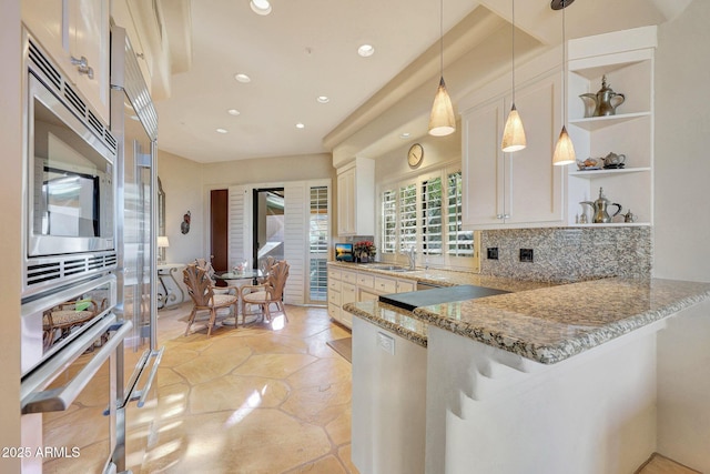 kitchen featuring white cabinetry, hanging light fixtures, light stone counters, kitchen peninsula, and appliances with stainless steel finishes