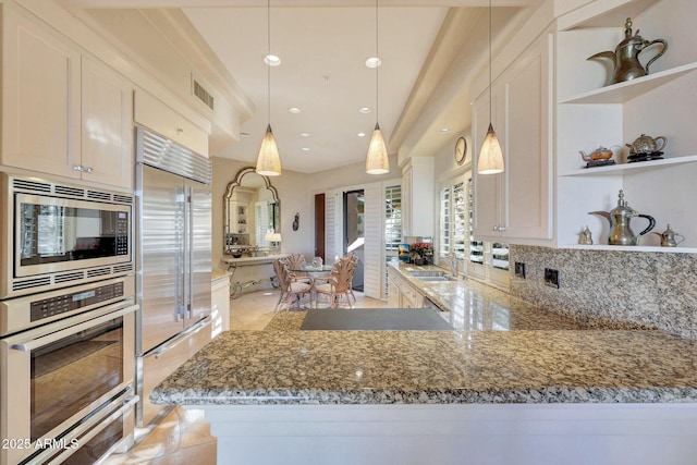 kitchen with built in appliances, pendant lighting, white cabinetry, and sink