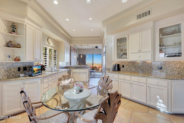 kitchen with ceiling fan, sink, light stone counters, backsplash, and white cabinets