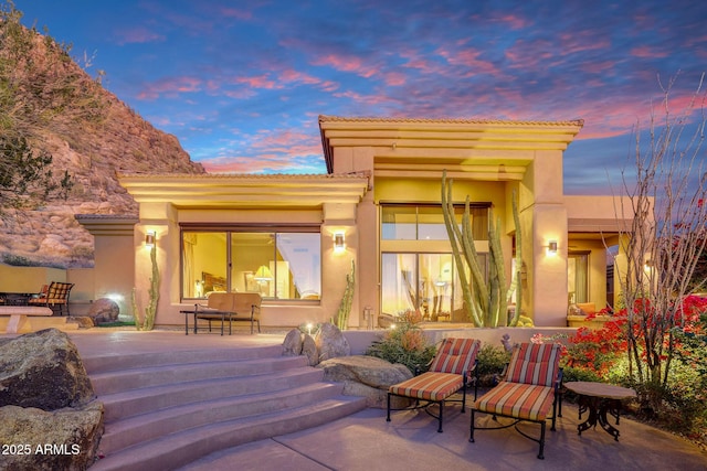 back house at dusk featuring a patio