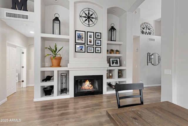 living room with hardwood / wood-style floors, built in features, and a large fireplace