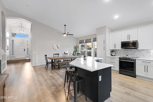 kitchen featuring white cabinetry, vaulted ceiling, light hardwood / wood-style flooring, an island with sink, and range with electric cooktop