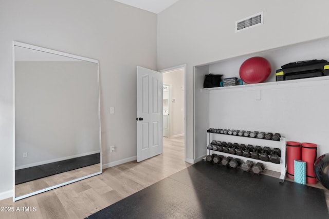 workout room with a towering ceiling and light hardwood / wood-style flooring