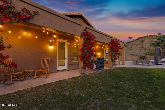 back house at dusk with a yard and a patio