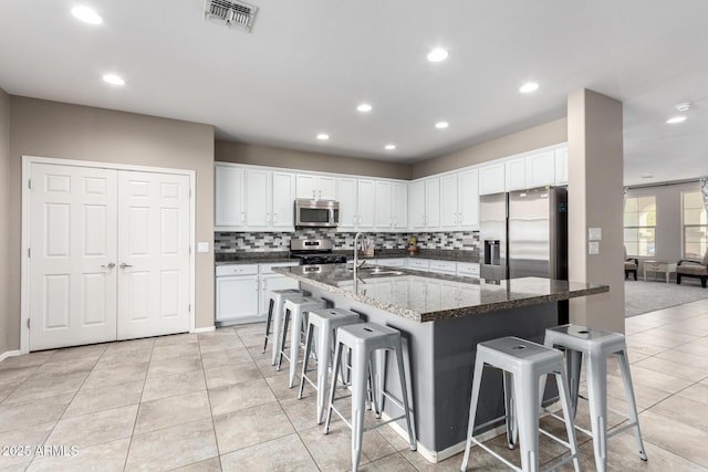 kitchen with visible vents, appliances with stainless steel finishes, a kitchen island with sink, white cabinets, and a kitchen bar