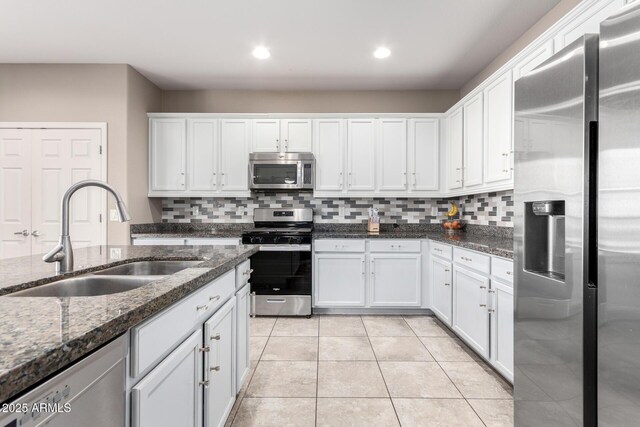 kitchen with dark stone counters, appliances with stainless steel finishes, a sink, and white cabinetry