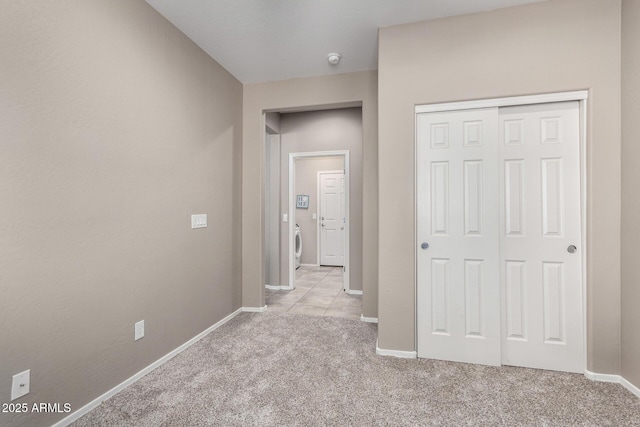 corridor with baseboards, washer / clothes dryer, and light colored carpet