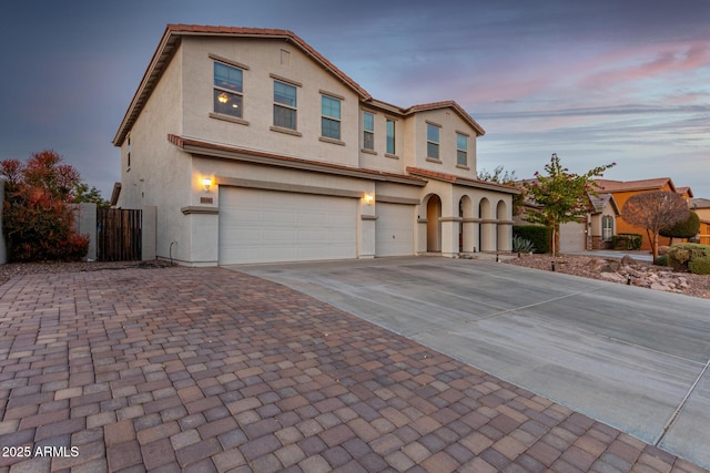 view of front of property featuring an attached garage, fence, a tile roof, driveway, and stucco siding