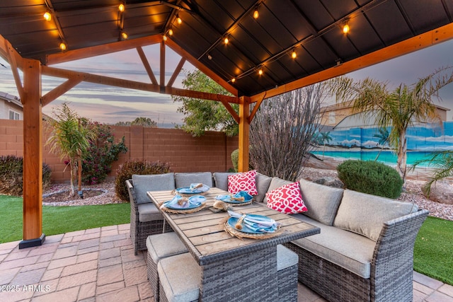 patio terrace at dusk featuring outdoor dining area, a fenced backyard, and a gazebo