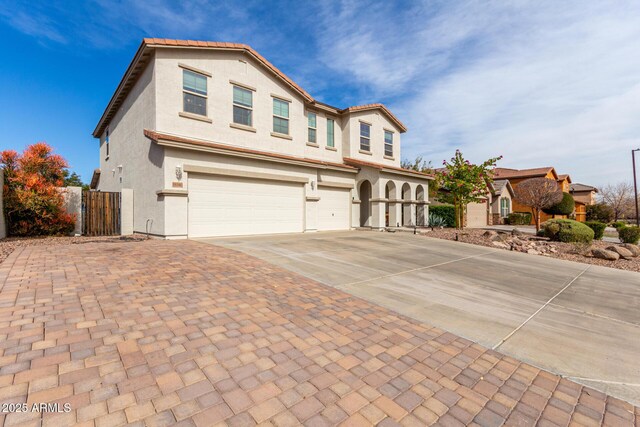 view of front facade with an attached garage, fence, driveway, a tiled roof, and stucco siding