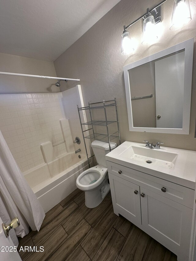 bathroom with wood finished floors, vanity, a textured wall, toilet, and bathing tub / shower combination