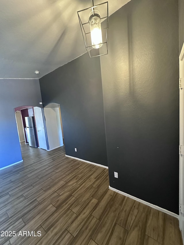 unfurnished room with baseboards, wood finished floors, and arched walkways