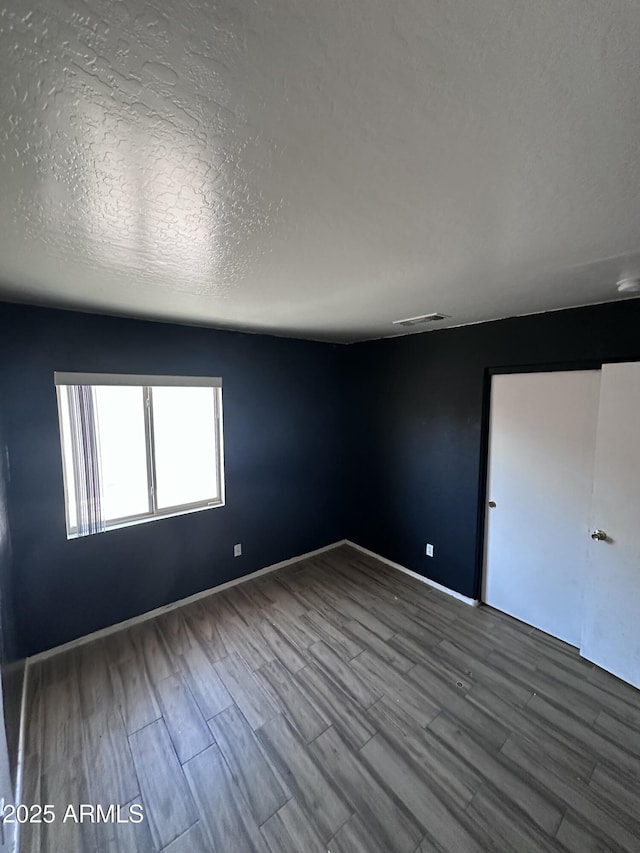 spare room featuring wood finished floors, a textured ceiling, baseboards, and visible vents