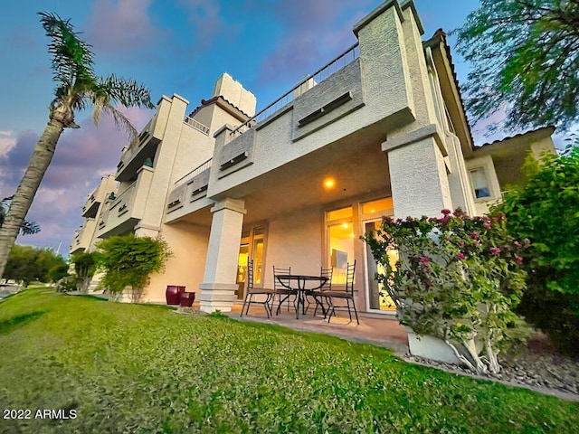 back house at dusk featuring a lawn and a patio area