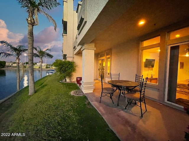 yard at dusk featuring a water view, a patio, and french doors