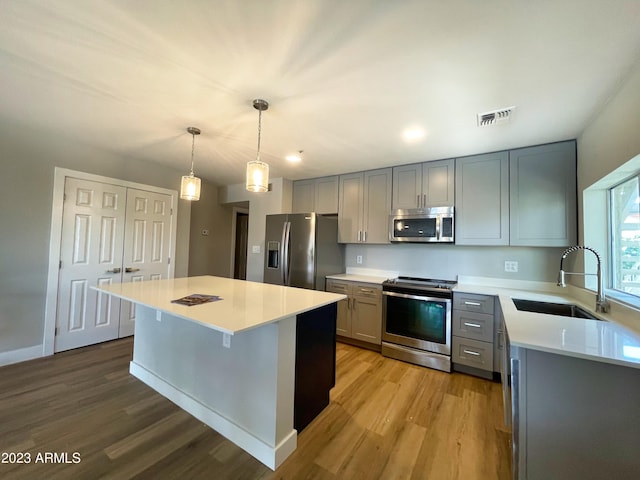 kitchen featuring pendant lighting, sink, light wood-type flooring, appliances with stainless steel finishes, and a kitchen island