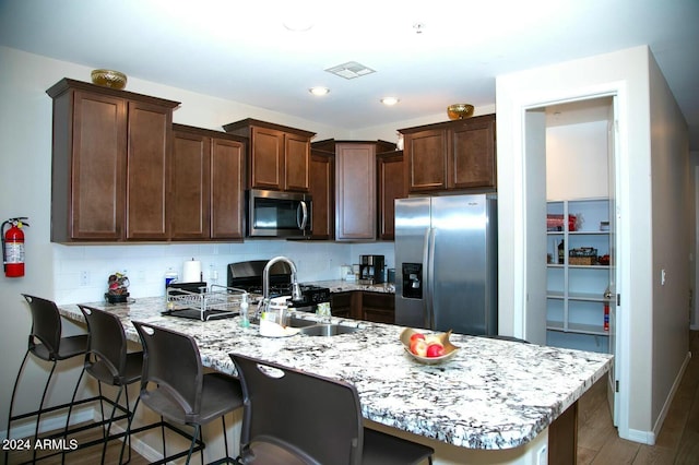 kitchen with decorative backsplash, appliances with stainless steel finishes, dark wood-type flooring, a breakfast bar area, and an island with sink