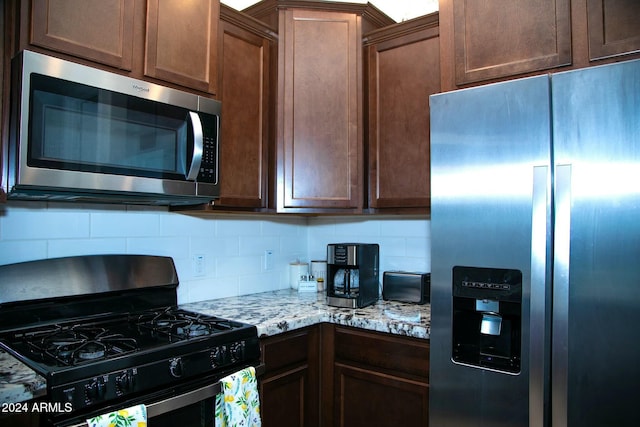 kitchen with backsplash, light stone counters, and appliances with stainless steel finishes