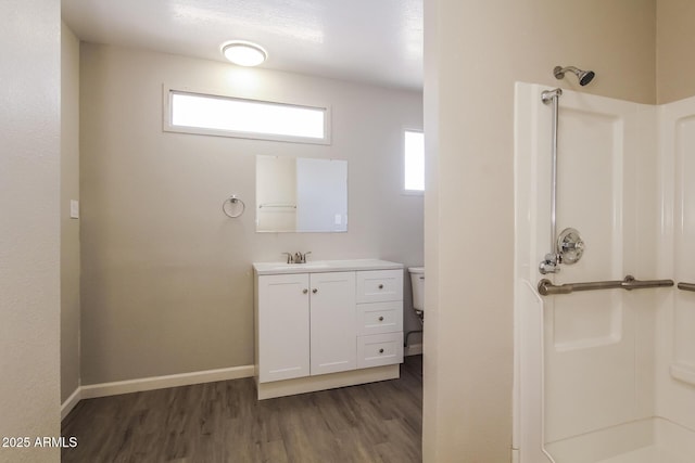 bathroom with wood finished floors, toilet, vanity, baseboards, and walk in shower