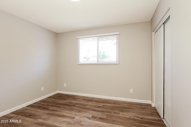 unfurnished bedroom featuring wood finished floors, a closet, and baseboards