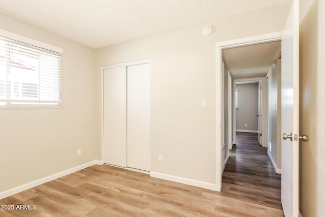 unfurnished bedroom with light wood-style floors, baseboards, a closet, and a textured ceiling
