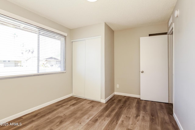 unfurnished bedroom featuring baseboards, wood finished floors, a textured ceiling, and a closet