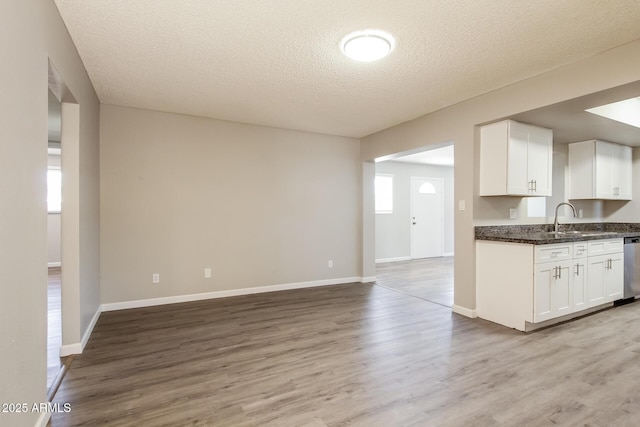 kitchen with stainless steel dishwasher, a textured ceiling, light wood-type flooring, open floor plan, and white cabinetry