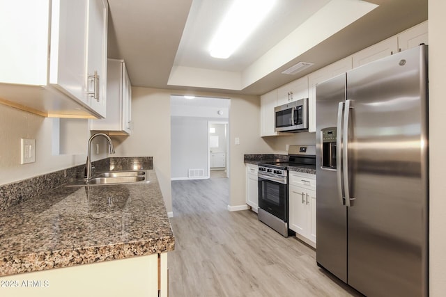 kitchen featuring a sink, light wood-style floors, stainless steel appliances, a raised ceiling, and visible vents