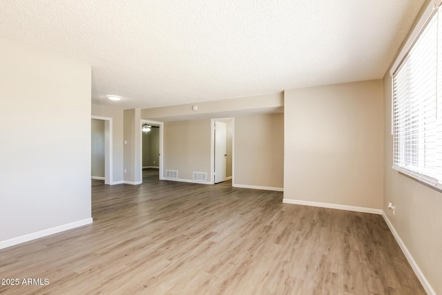 empty room with light wood-style floors, baseboards, visible vents, and a textured ceiling