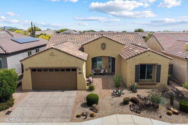 mediterranean / spanish home with a garage, stucco siding, a tiled roof, and concrete driveway