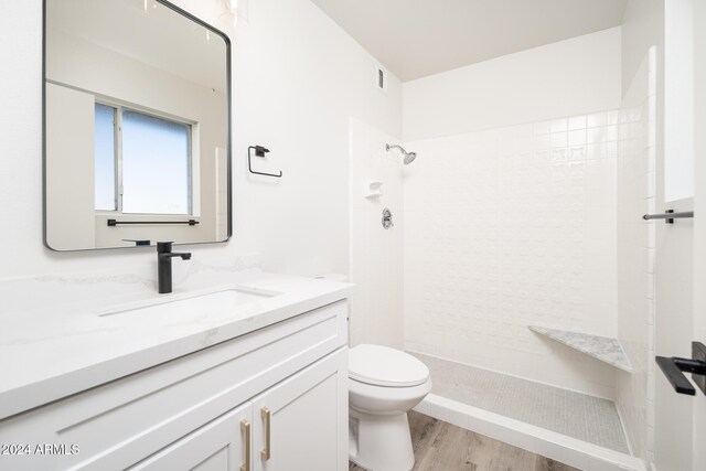 bathroom featuring hardwood / wood-style floors, vanity, toilet, and a tile shower