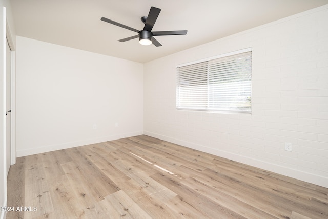 empty room with light hardwood / wood-style floors, ceiling fan, and brick wall