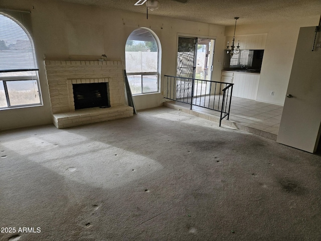 unfurnished living room featuring a fireplace, a textured ceiling, ceiling fan, and carpet flooring