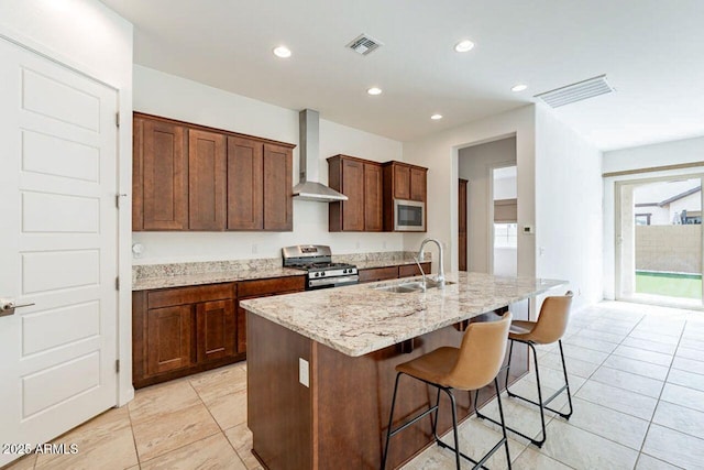 kitchen with visible vents, appliances with stainless steel finishes, wall chimney range hood, a kitchen island with sink, and a sink