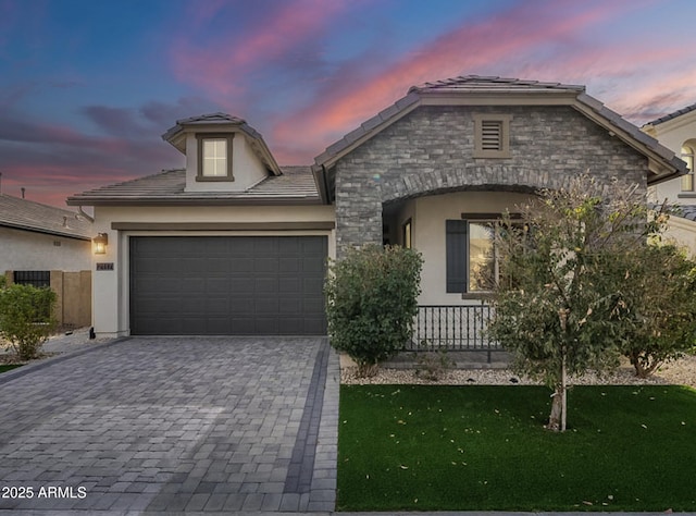 view of front of property featuring a lawn, stone siding, decorative driveway, stucco siding, and a garage