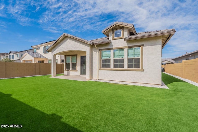 back of property featuring a tile roof, a lawn, a patio area, stucco siding, and a fenced backyard