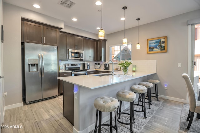 kitchen with visible vents, appliances with stainless steel finishes, a breakfast bar, a peninsula, and light countertops