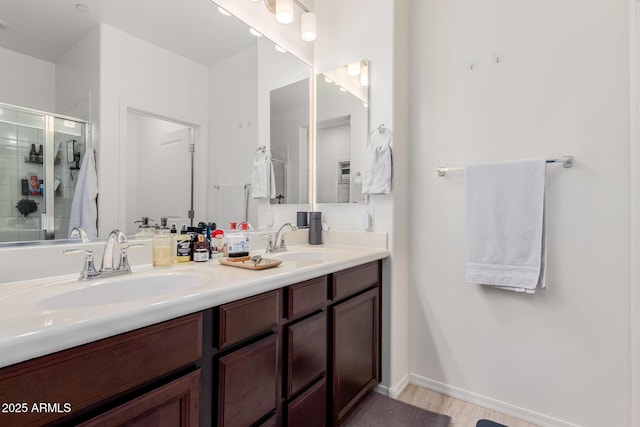 full bath with a stall shower, double vanity, baseboards, and wood finished floors