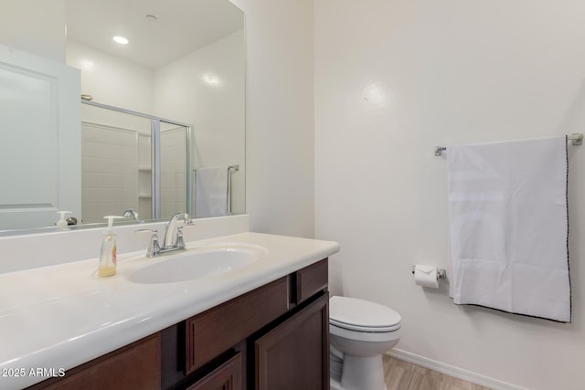 bathroom with a shower stall, toilet, vanity, baseboards, and wood finished floors