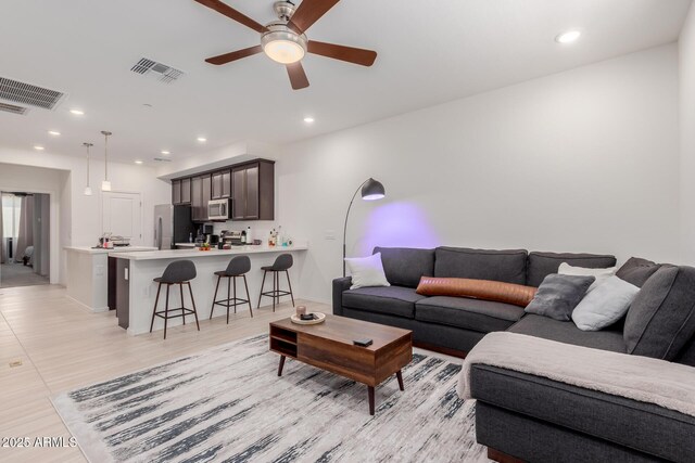living room featuring ceiling fan, recessed lighting, baseboards, and light wood-style flooring