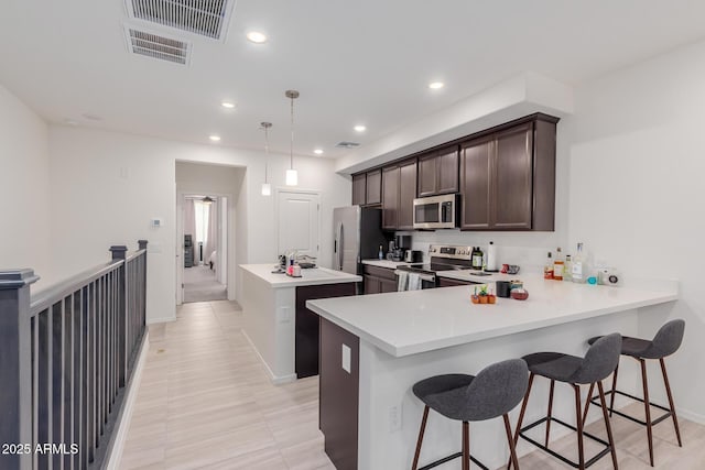 kitchen featuring stainless steel appliances, dark brown cabinetry, a kitchen island, baseboards, and light countertops