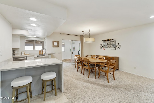 kitchen featuring a sink, a breakfast bar area, stainless steel dishwasher, light colored carpet, and white cabinets