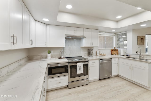 kitchen featuring white cabinetry, a sink, light stone counters, and appliances with stainless steel finishes