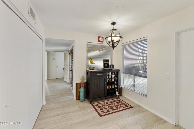 interior space featuring baseboards, light wood-style flooring, visible vents, and an inviting chandelier
