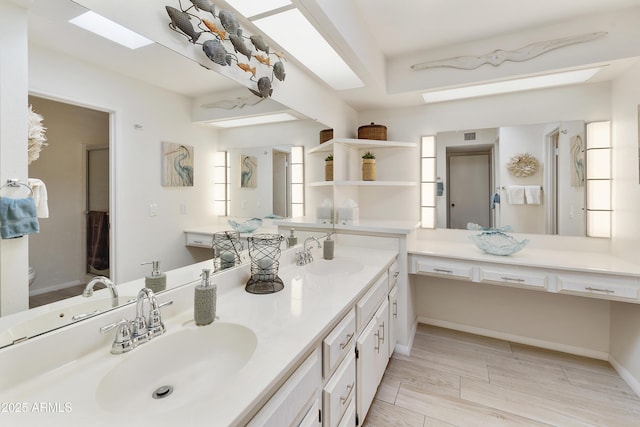 bathroom featuring double vanity, a sink, a skylight, and baseboards