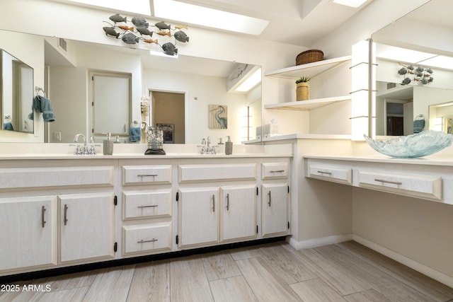 bathroom with a sink, wood finished floors, a skylight, visible vents, and double vanity