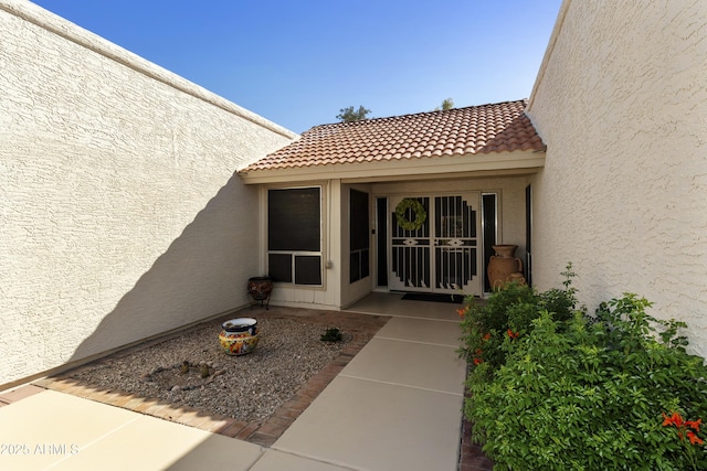 doorway to property featuring a tile roof, stucco siding, and a patio