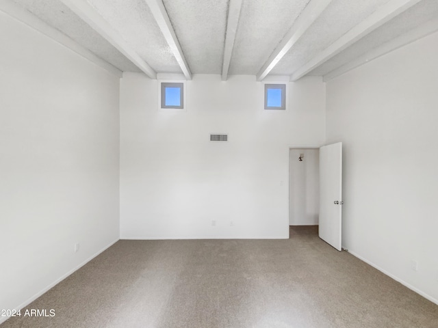 carpeted empty room with beamed ceiling, a healthy amount of sunlight, and a textured ceiling